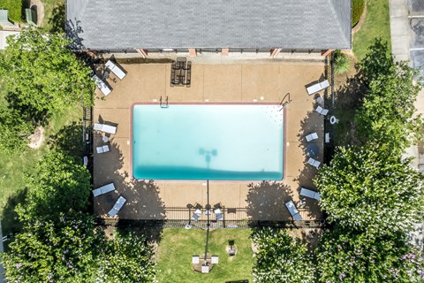 An aerial view of a swimming pool surrounded by trees and a building.