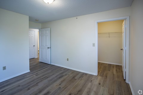 A room with white walls and wood flooring, with two doors and one open to a hallway.