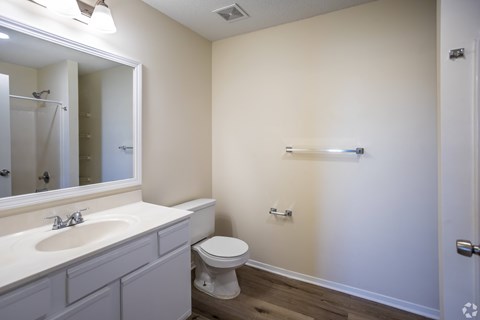 A bathroom with a toilet, sink, mirror, and a towel bar.