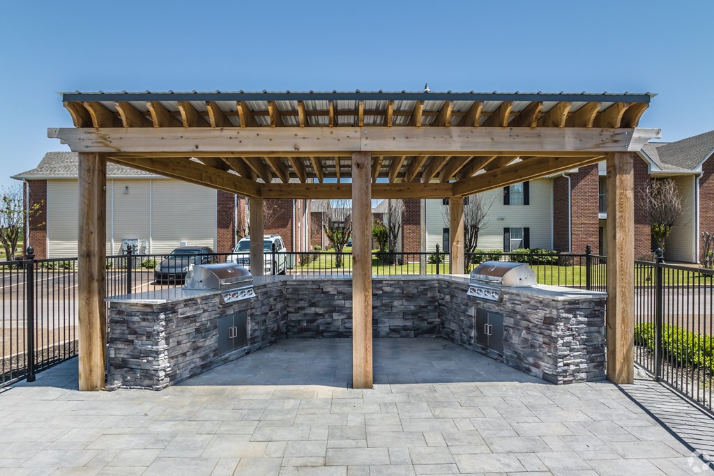 A wooden pergola with a stone base is in the foreground of a residential area.