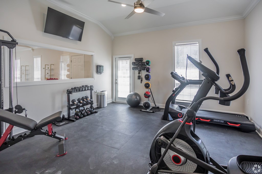 A home gym with a variety of exercise equipment including a treadmill, a rowing machine, and a bench press.