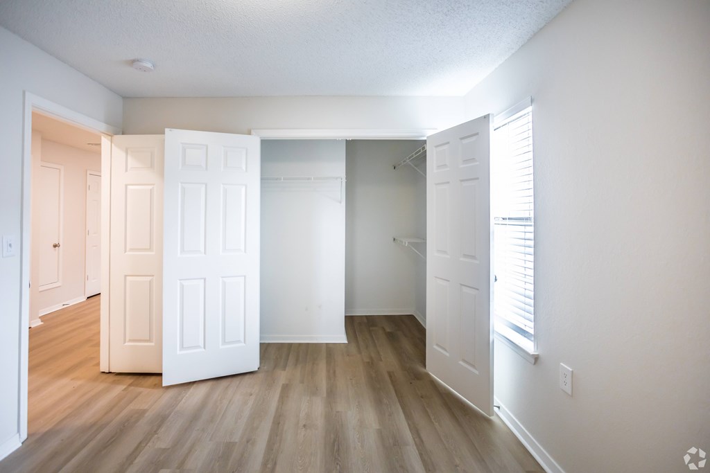 A room with white walls and wooden floors with a door open to another room.
