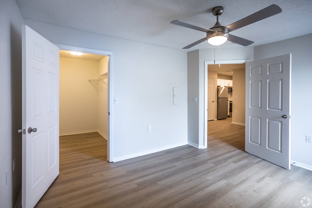 A room with a ceiling fan and light, two doors, and a wooden floor.