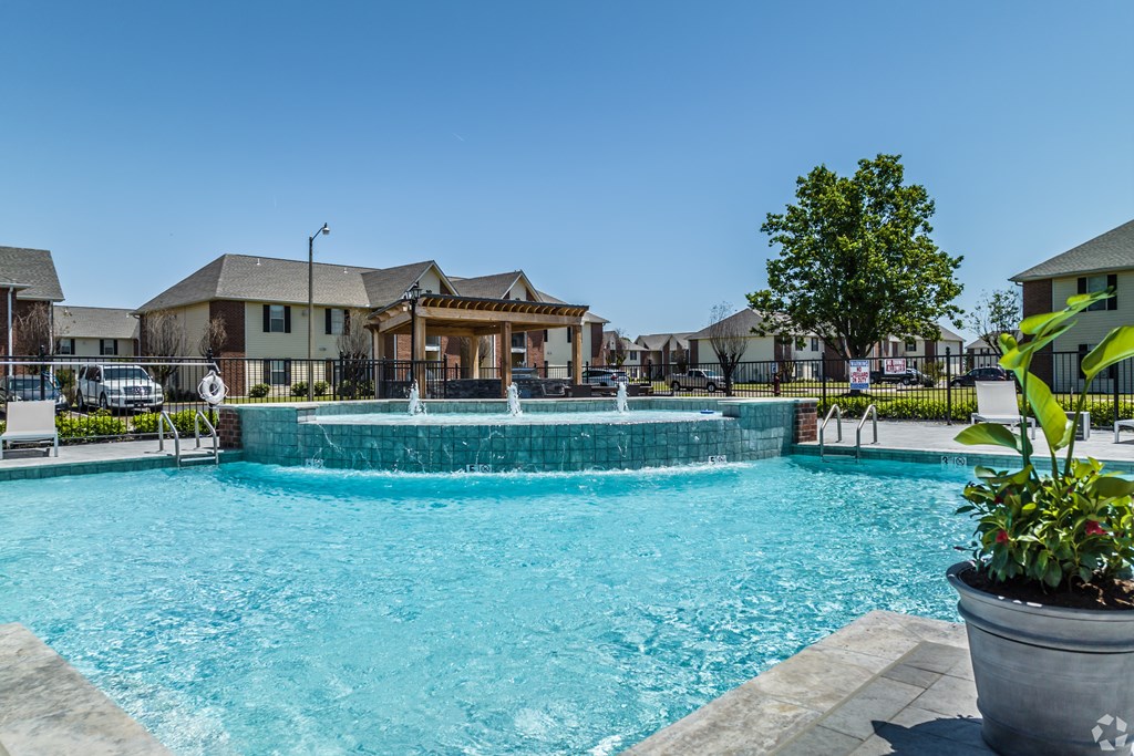 A swimming pool with a waterfall and a house in the background.