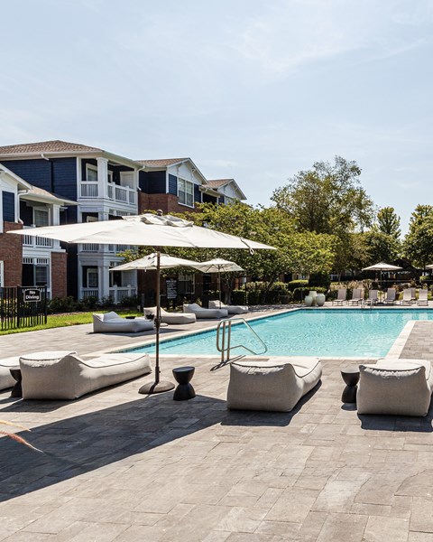 A pool surrounded by white cushioned chairs and umbrellas.