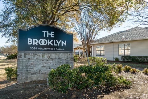 A sign for The Brooklyn apartment complex stands in front of a building.