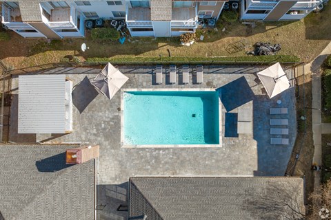 A swimming pool surrounded by a concrete patio and umbrellas.