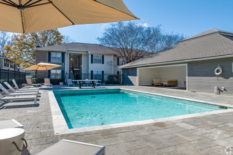 A pool with a yellow umbrella and a house in the background.