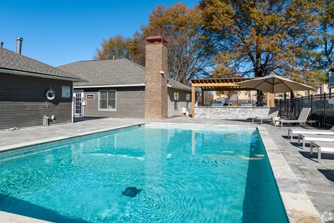A swimming pool in a backyard with a house and trees in the background.