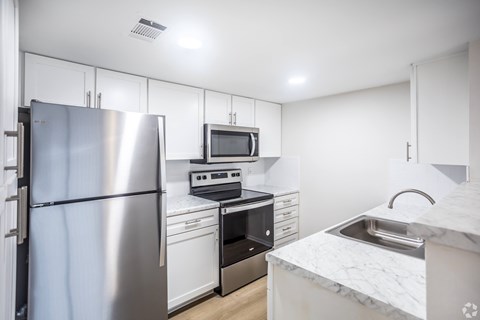 A kitchen with a refrigerator, microwave, oven, and sink.