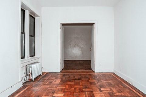 A room with a wooden floor and a white wall with a doorway.