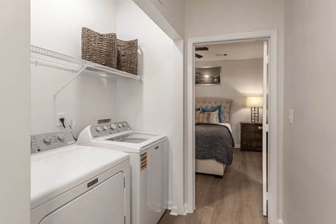 A laundry room with a washer and dryer and a bedroom with a bed and nightstand.