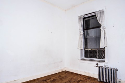 A window with a curtain and a radiator on a wooden floor.