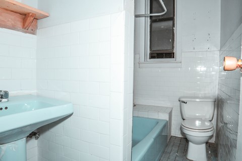 A white toilet sits next to a blue bathtub in a bathroom with white tiles.