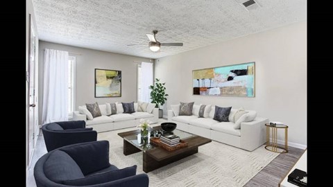 A living room with a white couch, a blue armchair, and a painting on the wall.