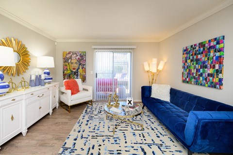 A blue couch sits in a living room with a white chair and a painting on the wall.