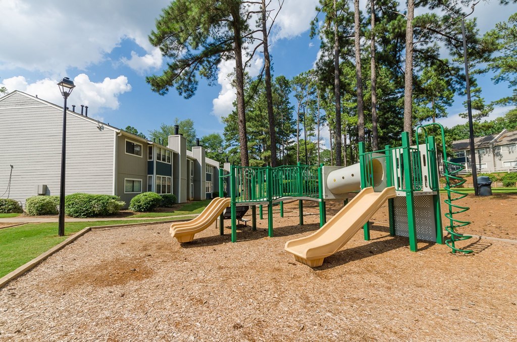 A playground with a yellow slide and green fencing.