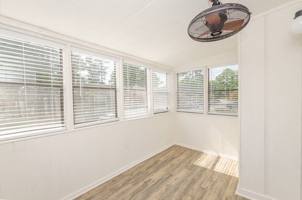 A room with a fan and three windows covered with blinds.