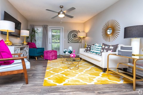 A living room with a white couch, a yellow rug, and a ceiling fan.