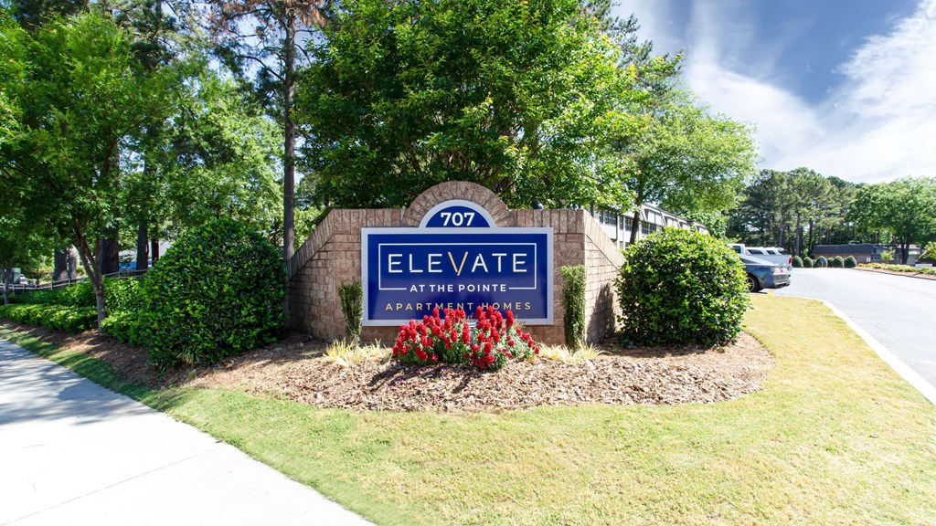 A sign for Elevate Apartments is surrounded by greenery and flowers.