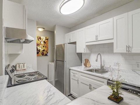 A kitchen with white cabinets and marble countertops.