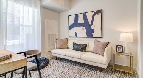 A living room with a white couch, a painting on the wall, and a small table with a lamp.