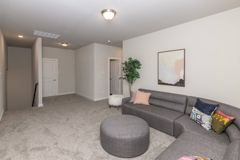 A living room with a grey couch and a round ottoman.