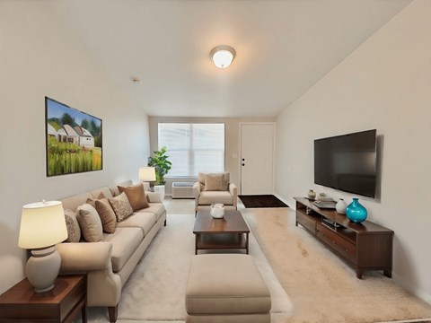 A living room with a beige sofa, a coffee table, and a flat screen TV mounted on the wall.