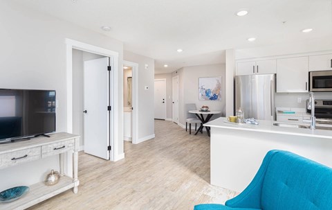 A blue chair is in the foreground of a white kitchen and living room.