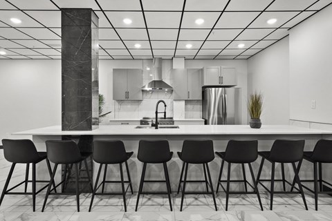 A modern kitchen with a white countertop and black barstools.