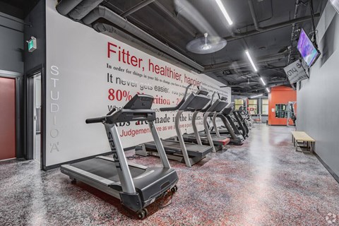 A gym with treadmills and a sign that says "Fitter, healthier, happier".