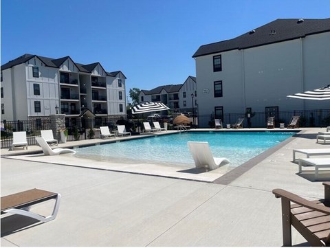 A swimming pool surrounded by lounge chairs and umbrellas in front of apartment buildings.