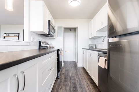 A modern kitchen with white cabinets and dark wood floors.