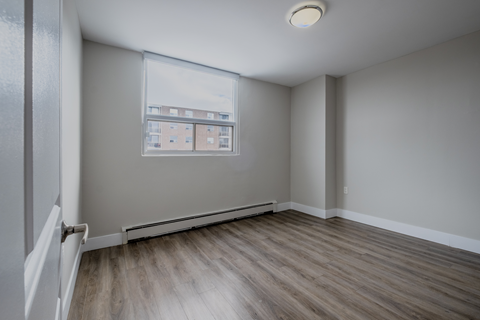 A room with a window and a view of a building across the street.