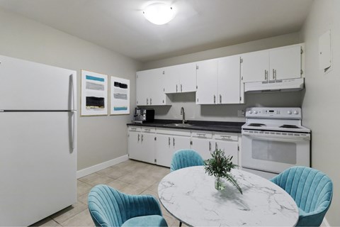 A kitchen with a white fridge, white cabinets, a white countertop, and a white island with a marble top.