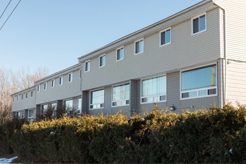 A building with grey siding and white trim is surrounded by a hedge.