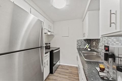 A modern kitchen with a stainless steel refrigerator and black countertops.
