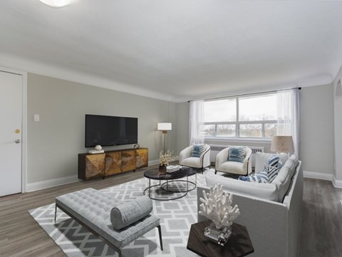 A living room with a grey couch, a grey ottoman, a black television, and a wooden side table.