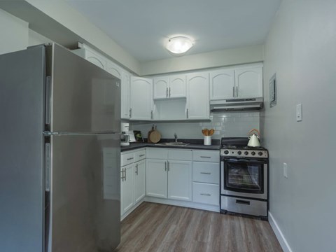 A kitchen with a stainless steel refrigerator and a stove with a pot on it.