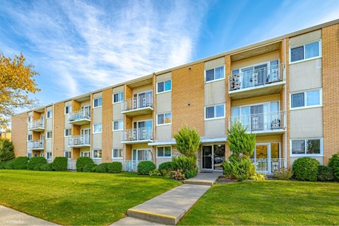 A row of apartment buildings with balconies and green lawns in front.