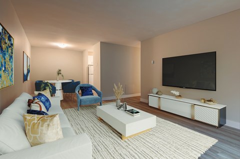 A living room with a white couch, a blue chair, a white coffee table, and a flat screen TV mounted on the wall.