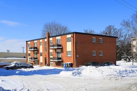 A red brick apartment building with snow on the ground and cars parked in front.