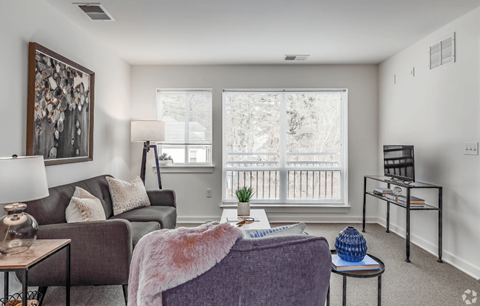 A living room with a grey couch, a purple chair, and a table with a blue vase on it.