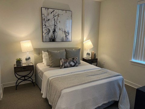 A bedroom with a bed, two lamps, and a painting on the wall.