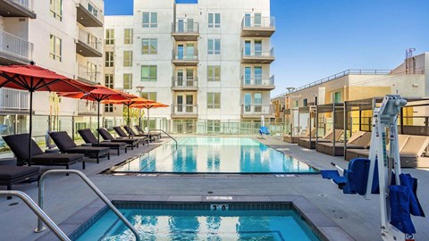 A swimming pool surrounded by lounge chairs and umbrellas in front of apartment buildings.