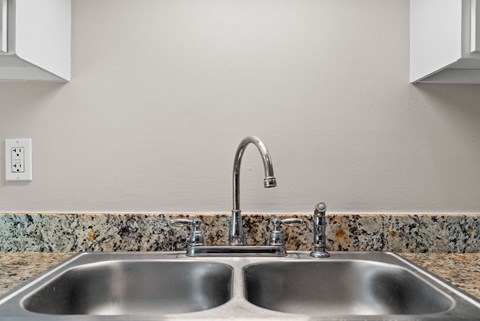 A kitchen sink with a chrome faucet and a granite countertop.