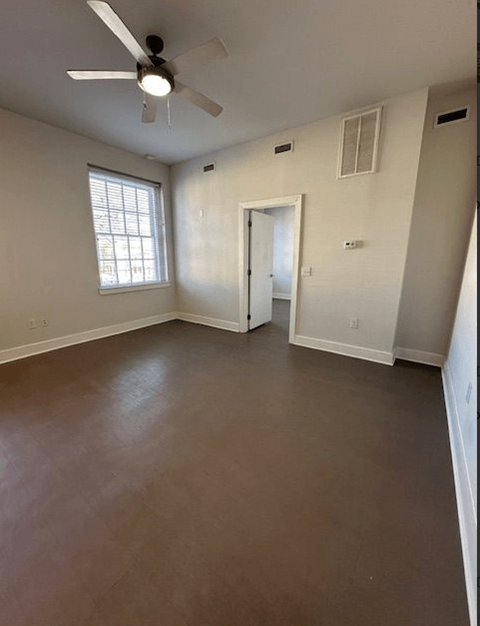 A room with a ceiling fan and brown flooring.