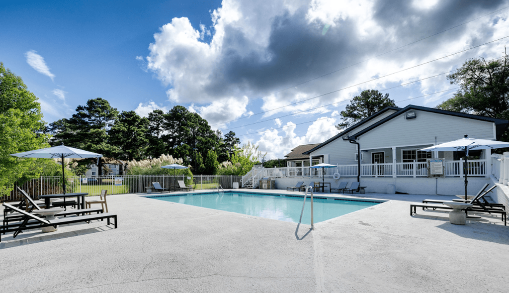 A swimming pool surrounded by a concrete patio and a white house at Retreat at Savannah Apartments, Savannah 31404