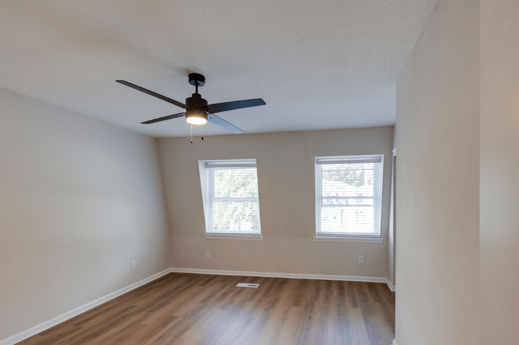 A room with a ceiling fan and two windows at Savan Pointe Apartments, Savannah