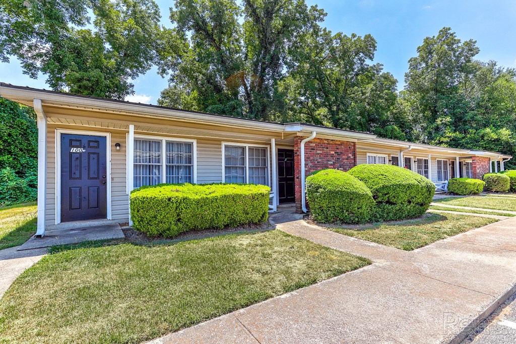 A row of residential buildings with bushes and a sidewalk in front.